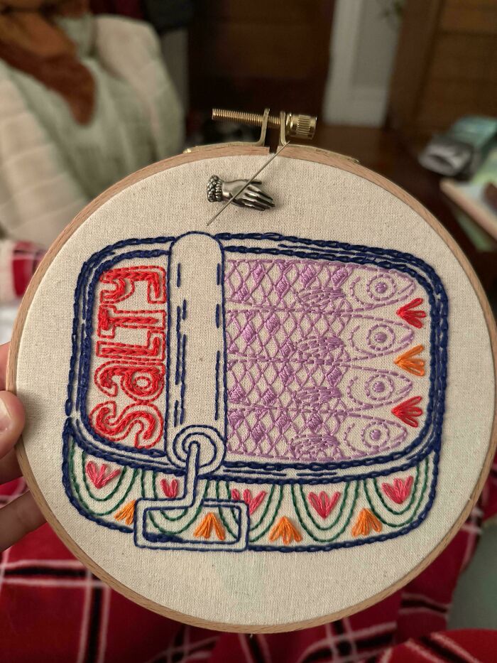 A charming embroidery creation depicting a sardine can with colorful fish and decorative patterns.