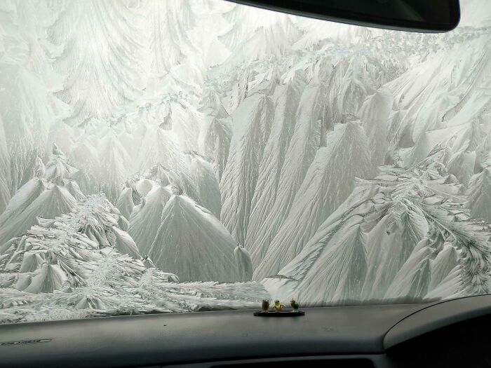 Frost patterns on a car windshield creating intricate, nature-inspired ice formations resembling mountains and valleys.