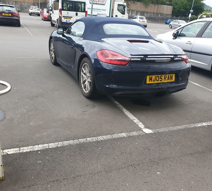 A luxury car parked over the line in a parking lot, showing lazy parking behavior and lack of effort.