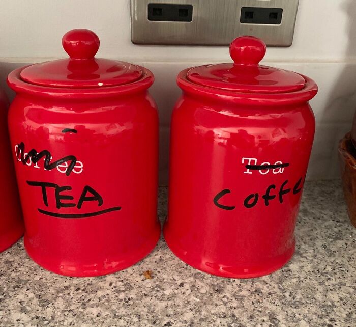 Red kitchen canisters labeled lazily with crossed-out words and corrected labels for tea and coffee.
