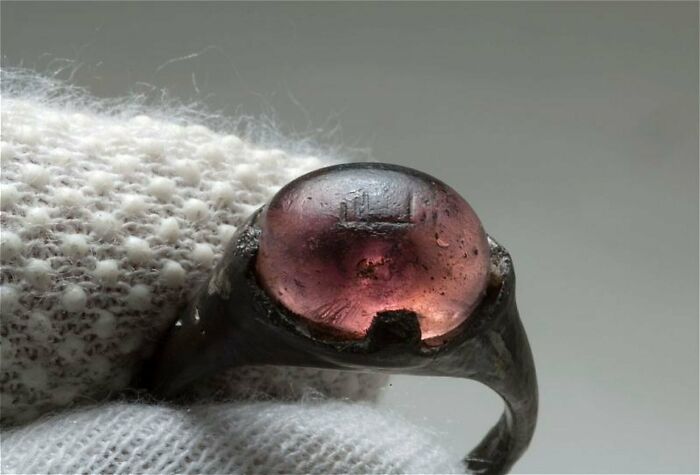 Close-up of an almost perfectly preserved antique ring with a pink gemstone held by a gloved hand, showcasing historical artifact.