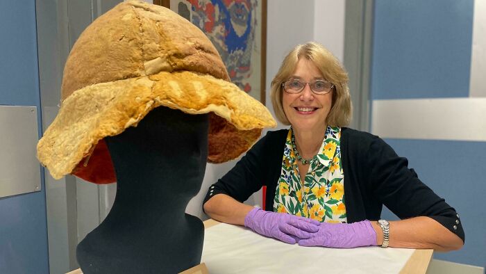 Woman wearing purple gloves showcasing an almost perfectly preserved antique hat, highlighting historical significance of the item.