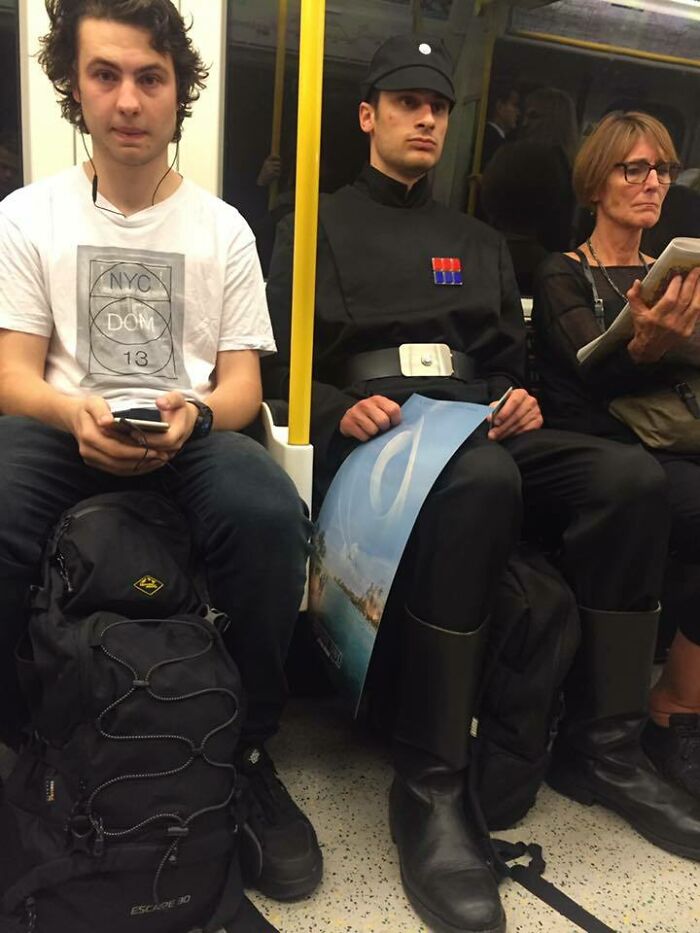Man dressed as Star Wars officer sitting on NYC subway next to casual passenger and woman reading a book during their ride.