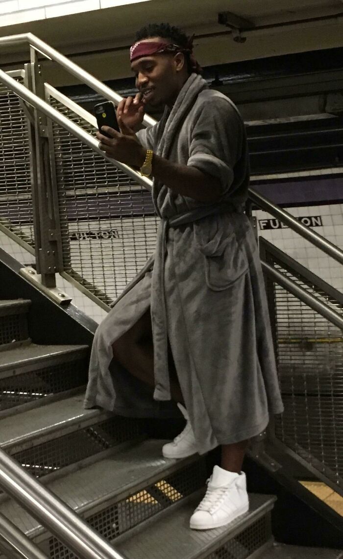 Man wearing gray robe and white sneakers taking a selfie on stairs in a NYC subway station with weird subway moments.
