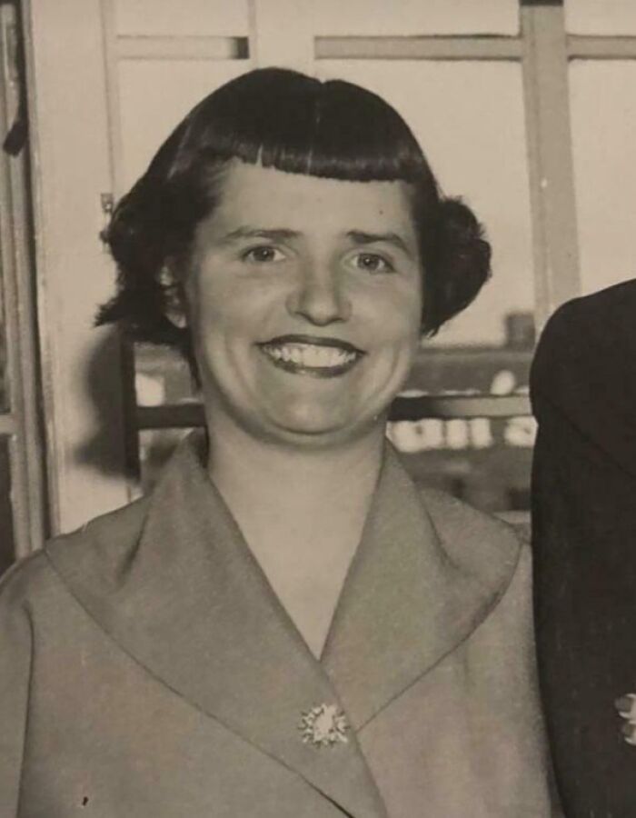 Woman with an uneven, tragic hair accident haircut smiling indoors, showcasing a hairstylist fail from a vintage photo.