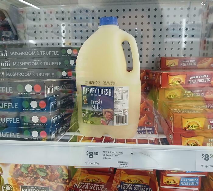 Plastic jug of fresh milk on a grocery shelf surrounded by frozen convenience foods in a lazy people's snack section.