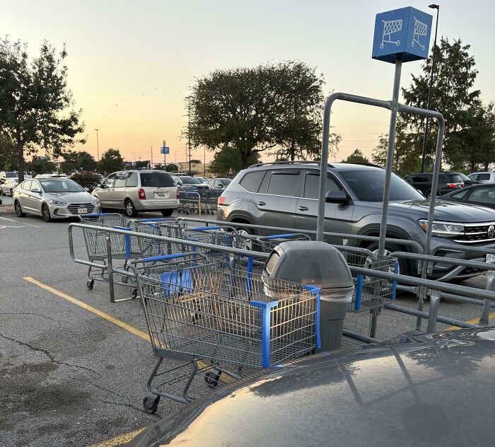 Shopping carts stacked awkwardly around a trash can in a parking lot, showing a humorous example of extreme laziness.