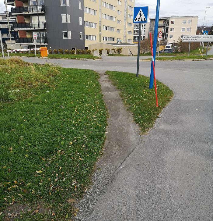 Worn footpath cutting across grass near a sidewalk, showing lazy shortcut between buildings and streets.