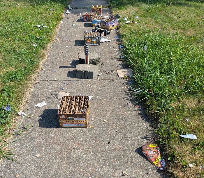 Firework boxes and debris left lazily scattered on a sidewalk, illustrating extreme laziness outdoors.