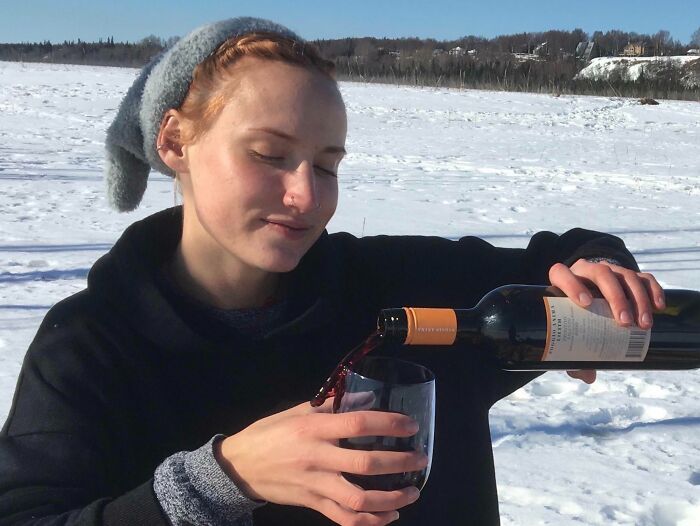 Woman pouring wine into glass outdoors in snowy landscape, capturing an unexpected better photo moment.