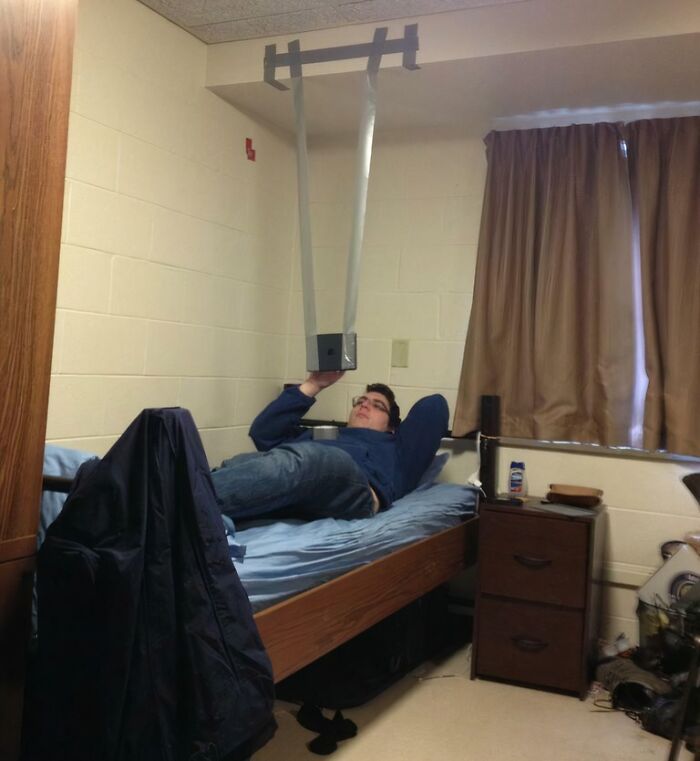 Person lying on bed using a homemade device to watch a phone hands-free, showing extreme laziness and creativity.
