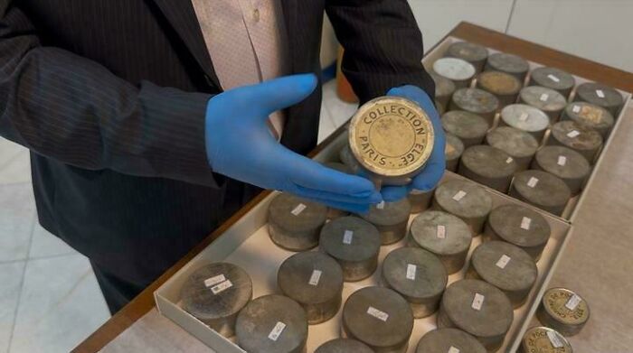 Person wearing blue gloves holding an antique metal canister from a collection of preserved historical items.