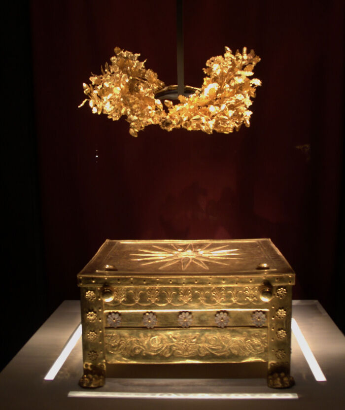 Antique golden chest and wreath displayed under light, showcasing almost perfectly preserved historical artifacts in a museum setting.