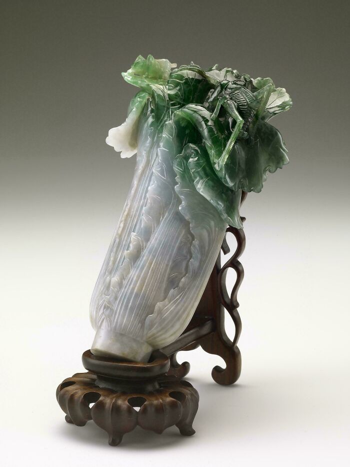 Antique jadeite cabbage sculpture with intricate carvings, displayed on a vintage wooden stand, showcasing almost perfectly preserved details.