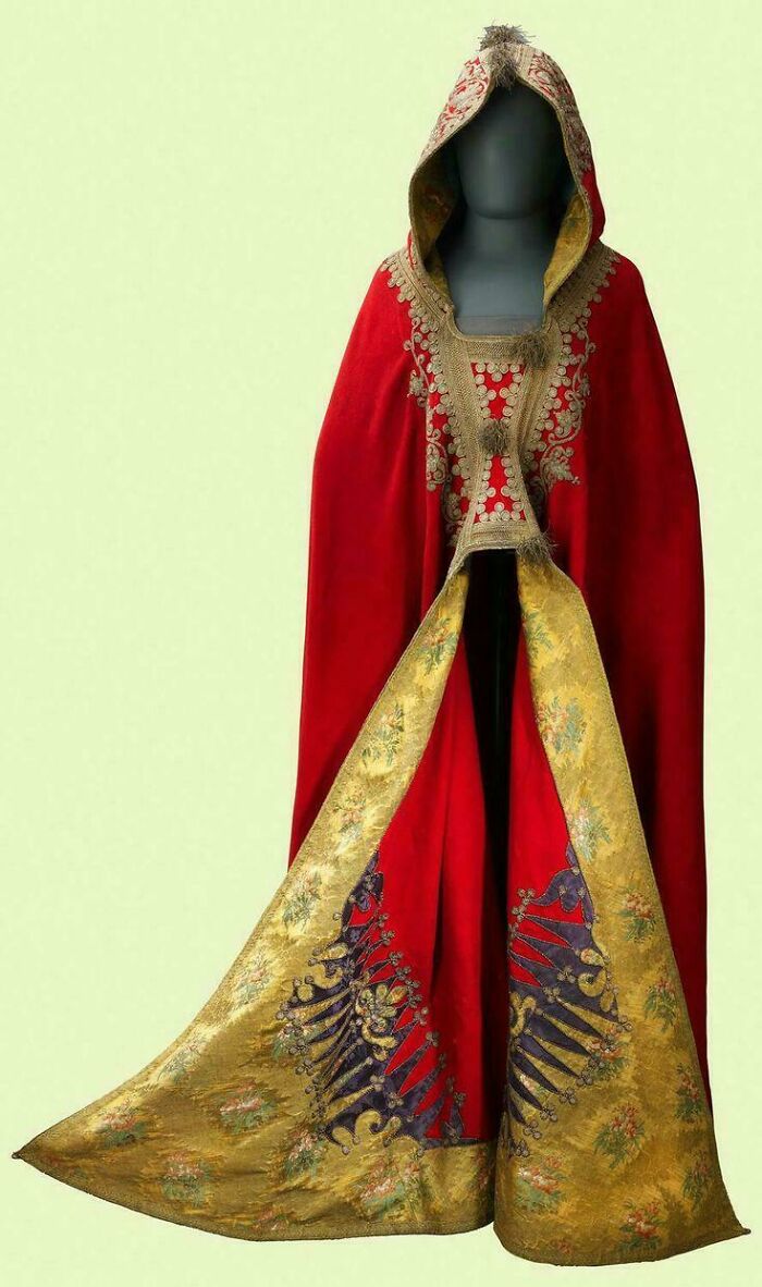 Antique red and gold embroidered cloak with hood displayed on a mannequin, showcasing historical preservation.