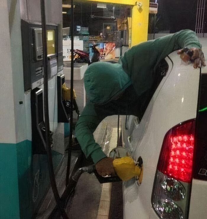 Person showing extreme laziness by reaching out of car window to pump gas at a fuel station late at night.