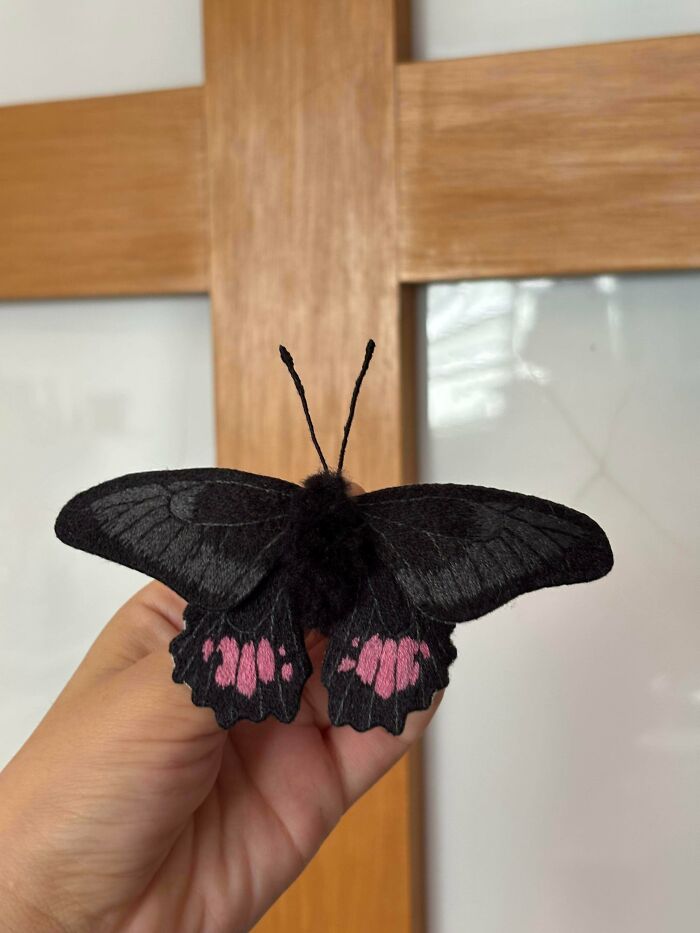 A hand holding a stunning black butterfly embroidery creation with pink accents on its wings.