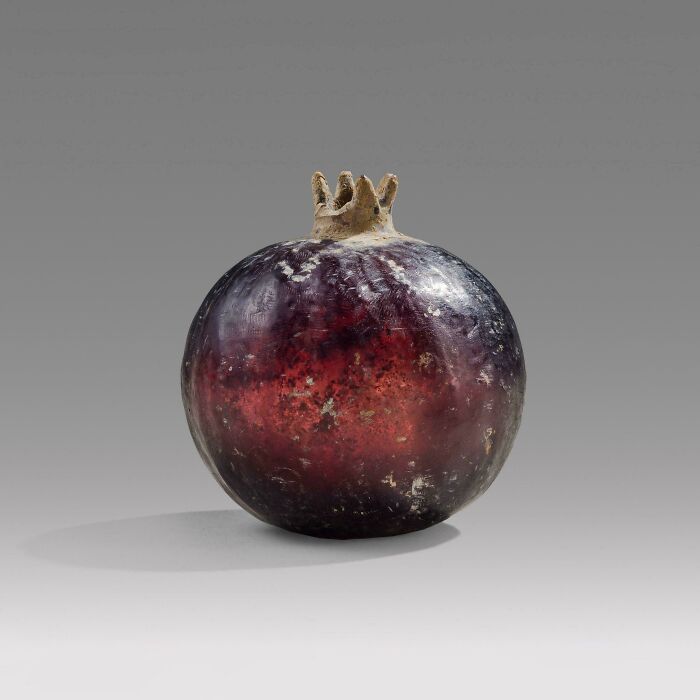 Almost perfectly preserved antique pomegranate artifact with deep red and purple hues against a plain gray background.