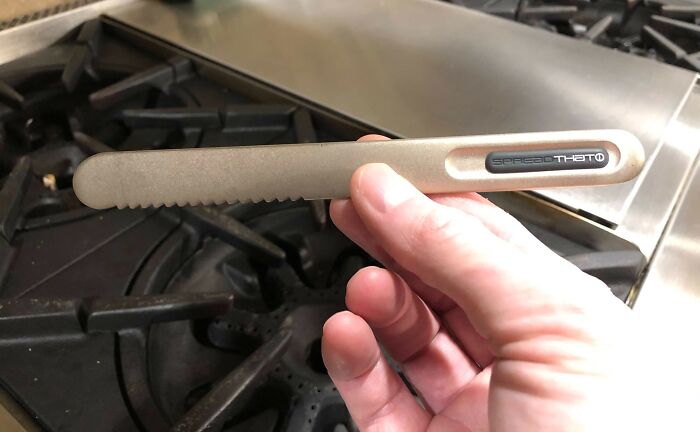 Hand holding a serrated utensil tool above a gas stove, showcasing an interesting tool for solving small kitchen problems.