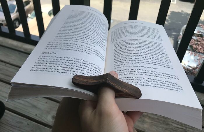 Hand holding an open book with a wooden finger book holder tool solving the problem of easy page turning.