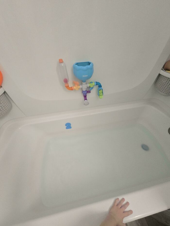 A great dad's view of a bathtub filled with water, a blue number 2, and a bath toy on the wall.