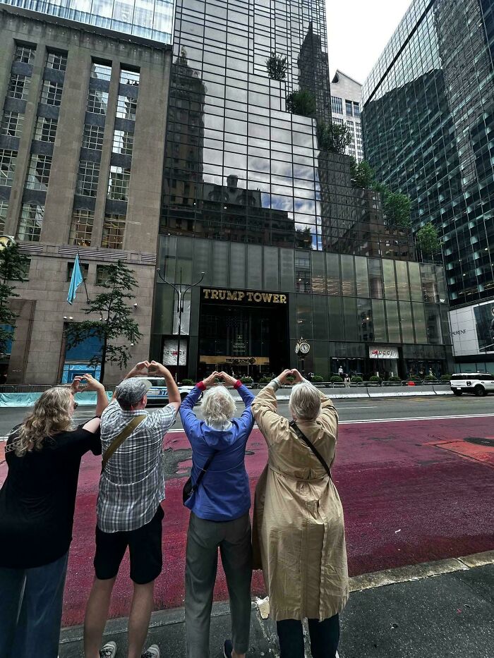 Four people making heart shapes with their arms facing Trump Tower, showing cringe moments captured in new pics.