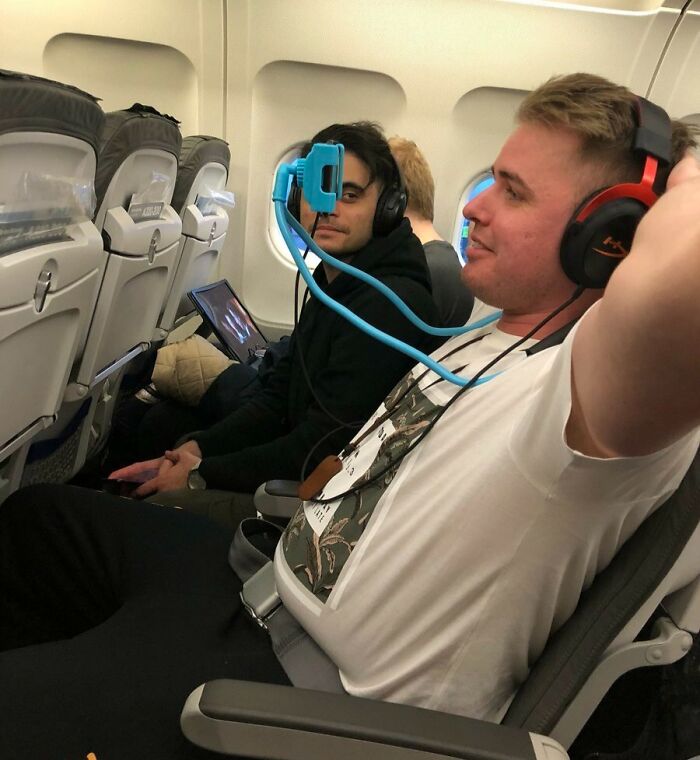 Two men on an airplane using a flexible phone holder, an interesting tool to solve small travel annoyances.