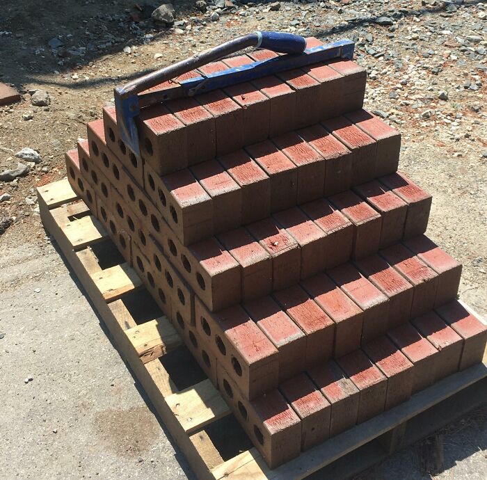 Brick carrying tool holding a stack of red bricks on a wooden pallet, an interesting tool to solve a common problem.