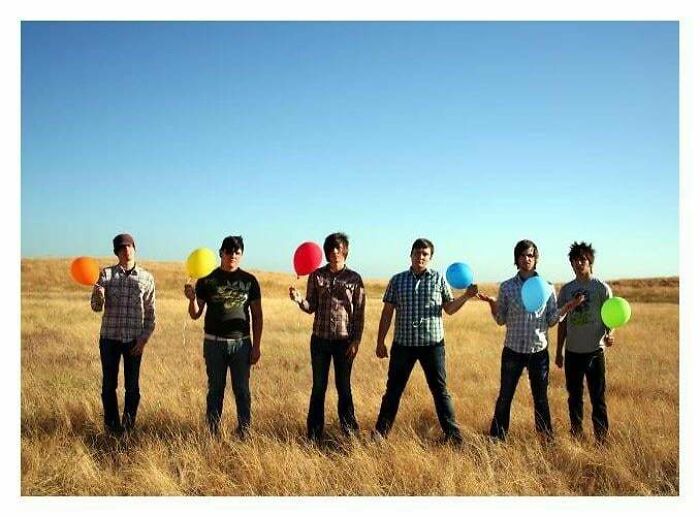 Six young men standing in a field holding colorful balloons, capturing a cringe moment in an outdoor setting.