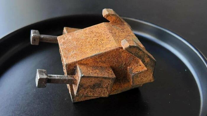 Rusty metal object with an unusual design showcasing metalworkers defying physics and logic on a black surface.