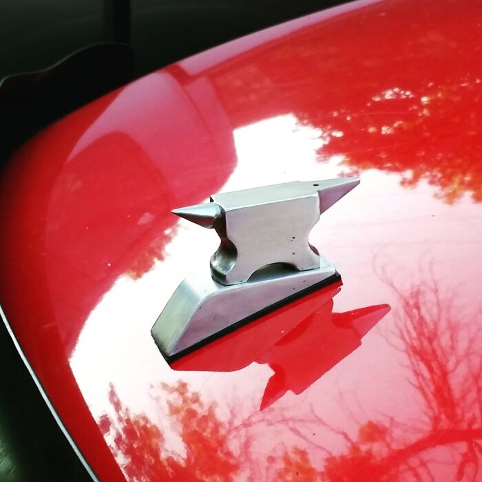 Small metal anvil sculpture mounted on a shiny red surface, showcasing skilled metalworkers' remarkable craftsmanship.