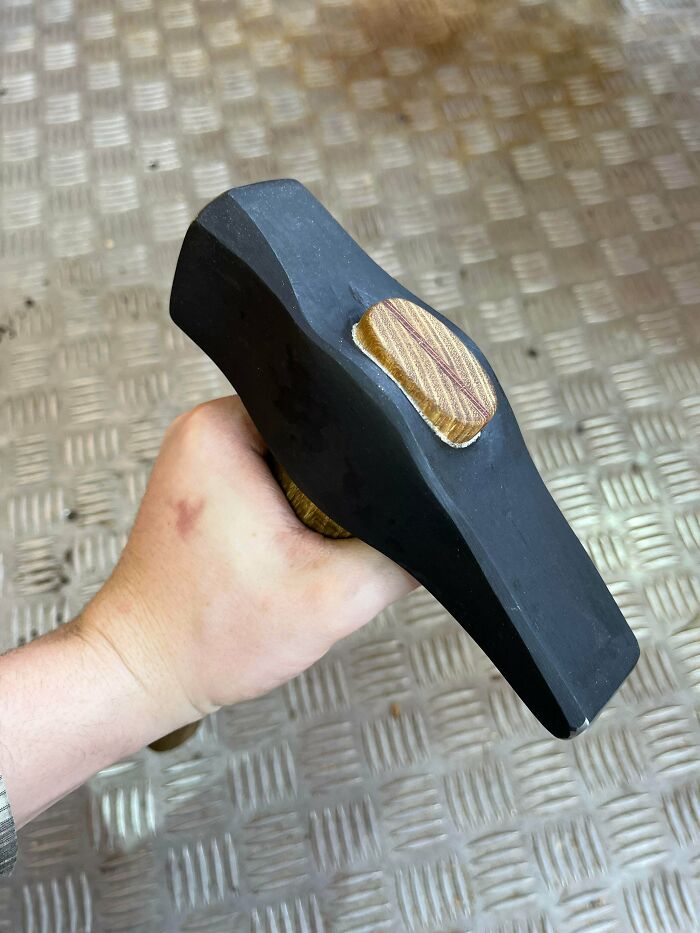 Hand holding a black metal hammer with a wooden face, showcasing remarkable metalworker craftsmanship and design.