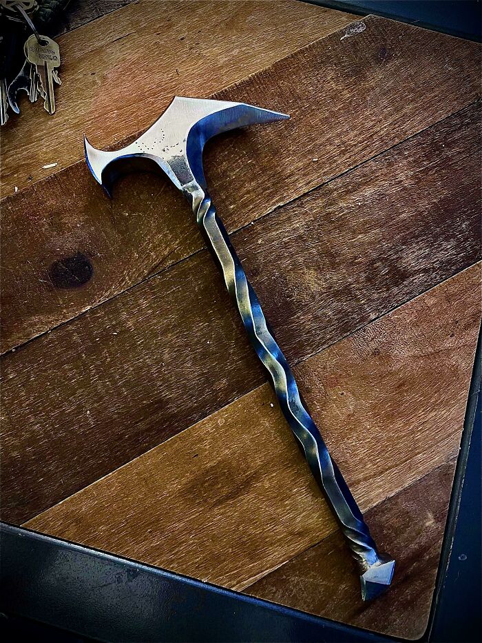 Twisted metal hammer with sharp, curved head showcasing metalworkers craftsmanship and remarkable design on wooden surface.