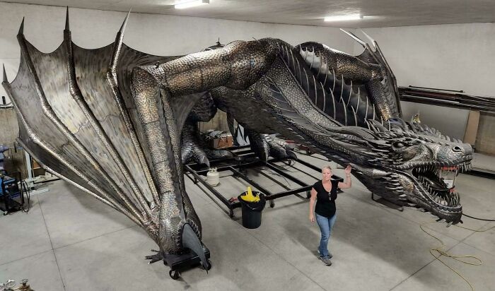 A large, detailed metal dragon sculpture inside a workshop, showcasing metalworkers defying physics and logic.