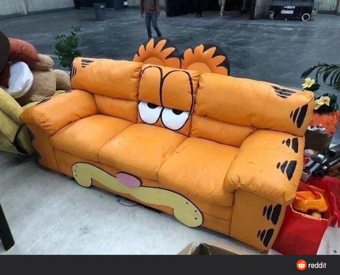 Orange couch designed like a cartoon character with expressive eyes and paw prints, a ridiculous piece of furniture spotted online.