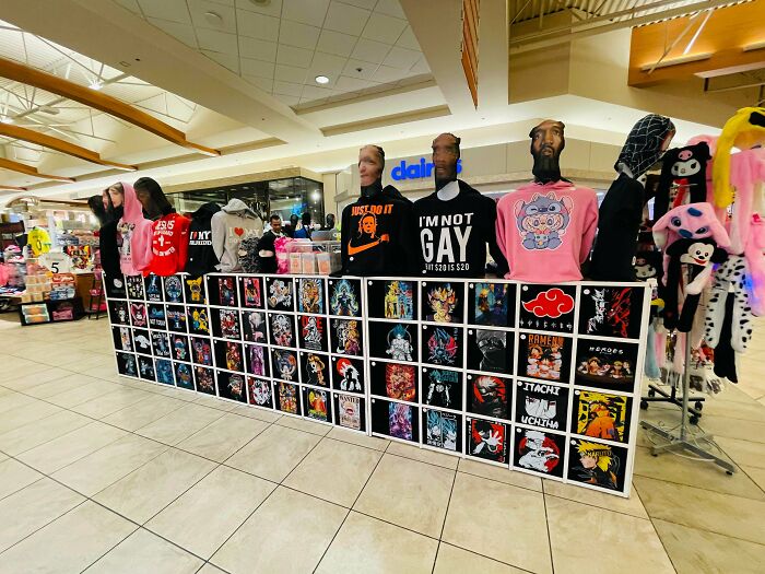 Display of cringe fashion and anime-themed apparel at a mall kiosk with mannequins wearing bold graphic hoodies.