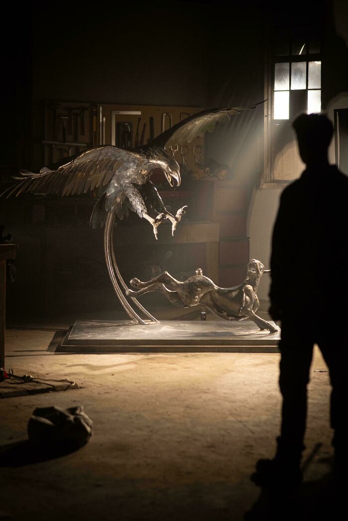 Metalworkers remarkable metal sculpture of an eagle attacking a dog, showcased in a workshop with dramatic lighting.