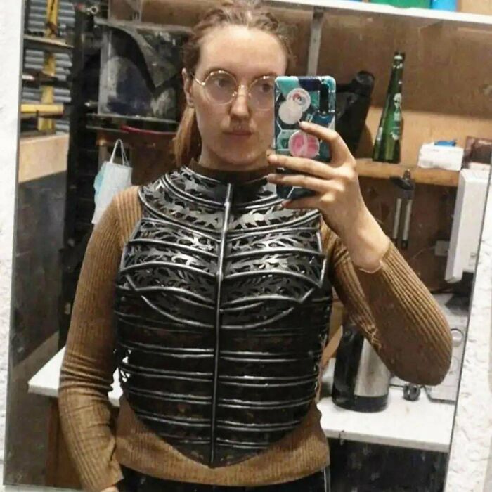 Woman wearing a detailed metal chest armor, showcasing metalworkers defying physics and logic with remarkable craftsmanship.