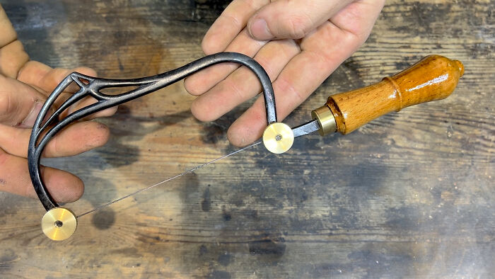 Handcrafted metalworking tool with a wooden handle and thin wire blade, showcasing metalworkers defying physics and logic.