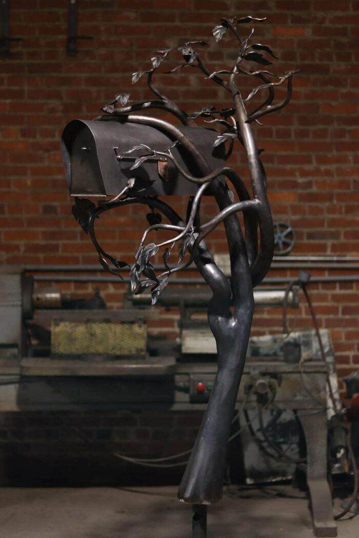 Metalworkers crafted a mailbox shaped like a tree with detailed branches and leaves in an industrial workshop setting.