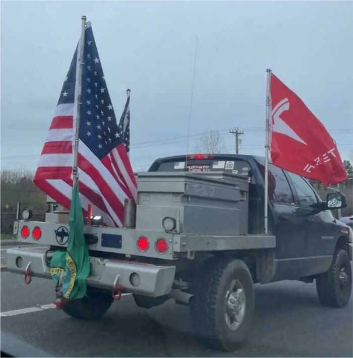 Pickup truck with multiple flags including American and Tesla flags, showcasing a cringe moment on the road.