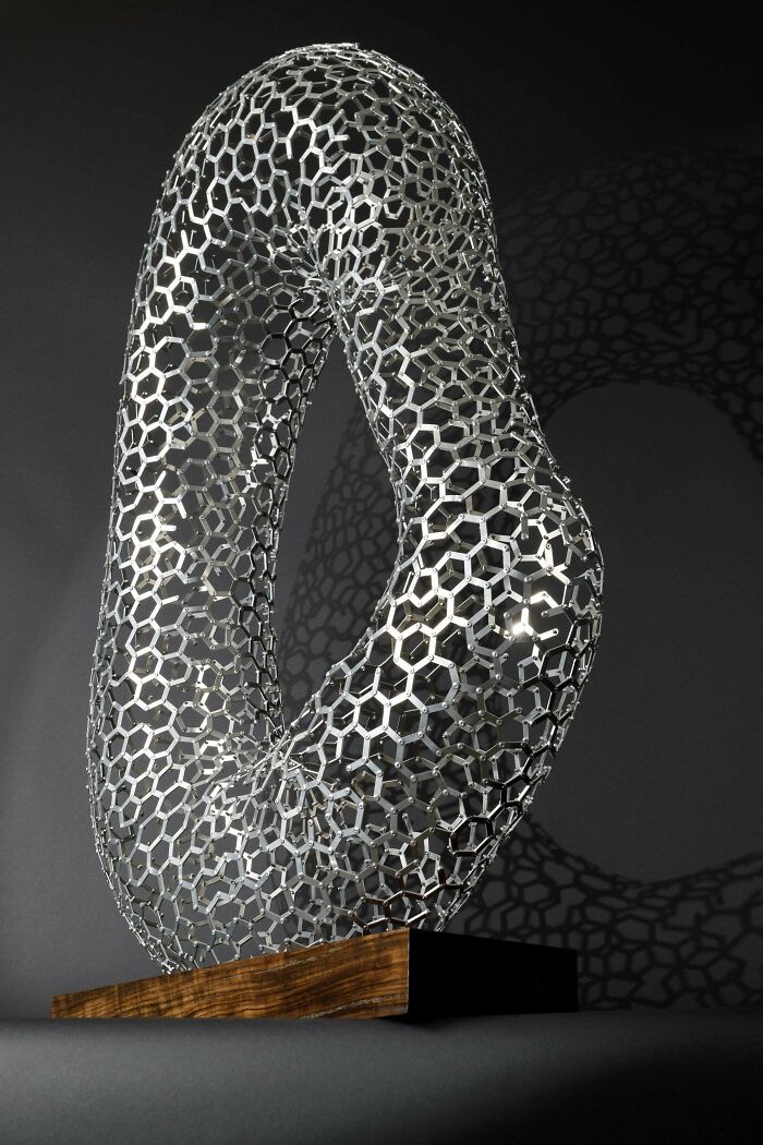 Intricate metal sculpture with hexagonal pattern on wooden base showcasing metalworkers' skill defying physics and logic.