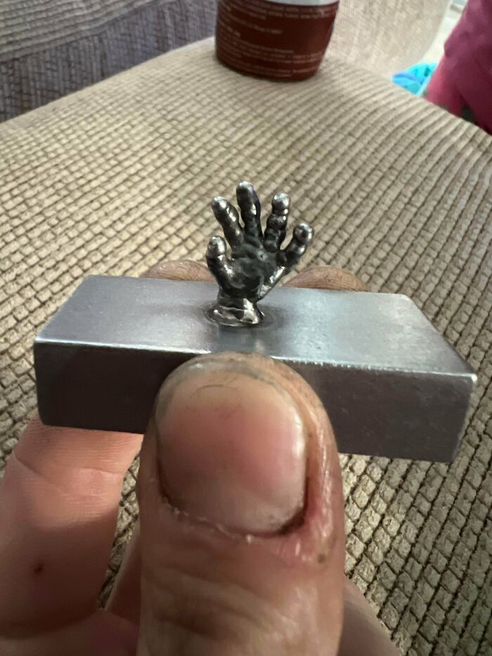 Tiny metal hand sculpture held between fingers, showcasing remarkable metalworkers' skill defying physics and logic.
