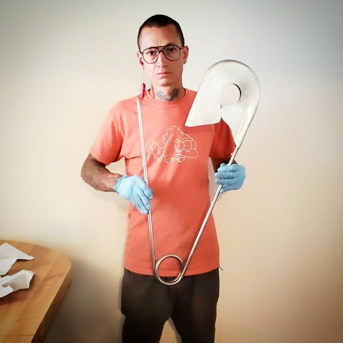 Man wearing gloves and glasses holding a large metal art piece, showcasing metalworkers defying physics and logic.