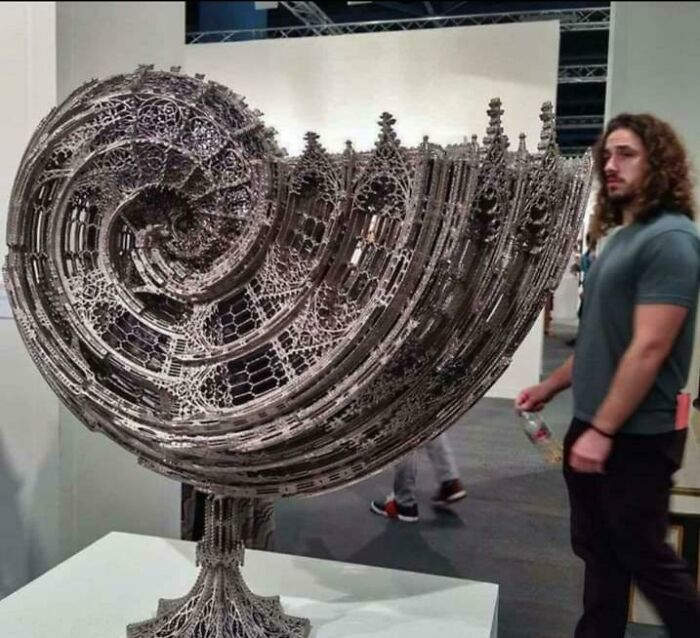 Intricate metal sculpture defying physics and logic, showcasing remarkable craftsmanship by skilled metalworkers in a gallery setting.