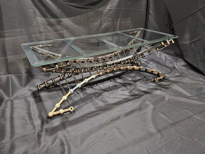 Metalworkers crafted a remarkable glass table featuring a complex, curved metal base resembling bike chains defying physics.