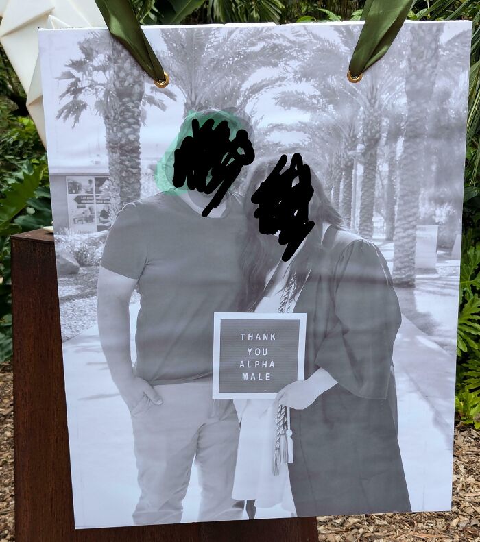 Couple posing with a cringe sign reading thank you alpha male in an outdoor setting with palm trees in the background