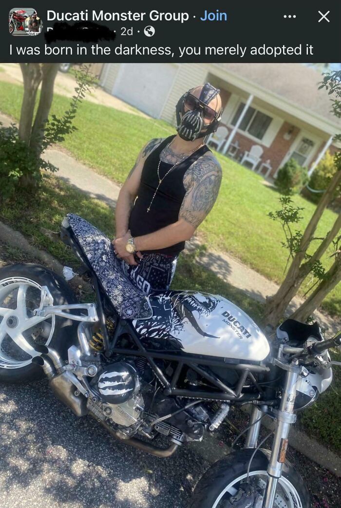 Man wearing a Bane mask and sunglasses posing with a customized Ducati Monster motorcycle outdoors.