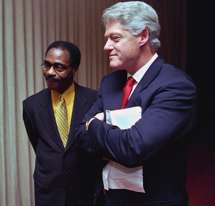 Two men in formal suits, one holding documents, representing celebrities falsely accused of horrible crimes.