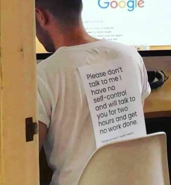 Man sitting at a desk with a humorous sign on his back, showing one of the strange signs that deserve a double take.